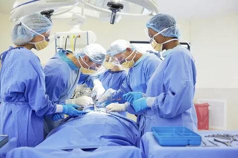 A team of surgeons in blue scrubs performing surgery on a patient in an operating room.