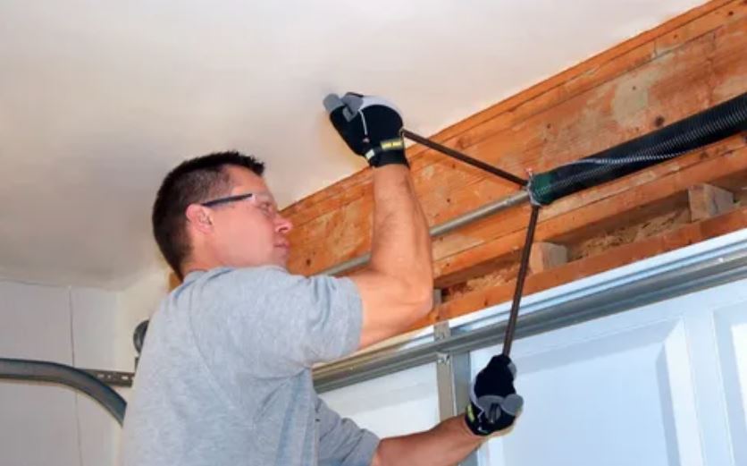 A man is diligently repairing a garage door, focused on his task in a well-lit garage environment.