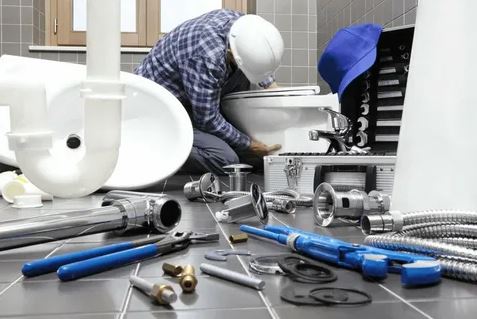 A man is repairing a toilet in a bathroom, focused on his task amidst the tiled surroundings.